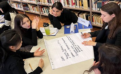 Students sit at a table in a library in Italy as one takes notes